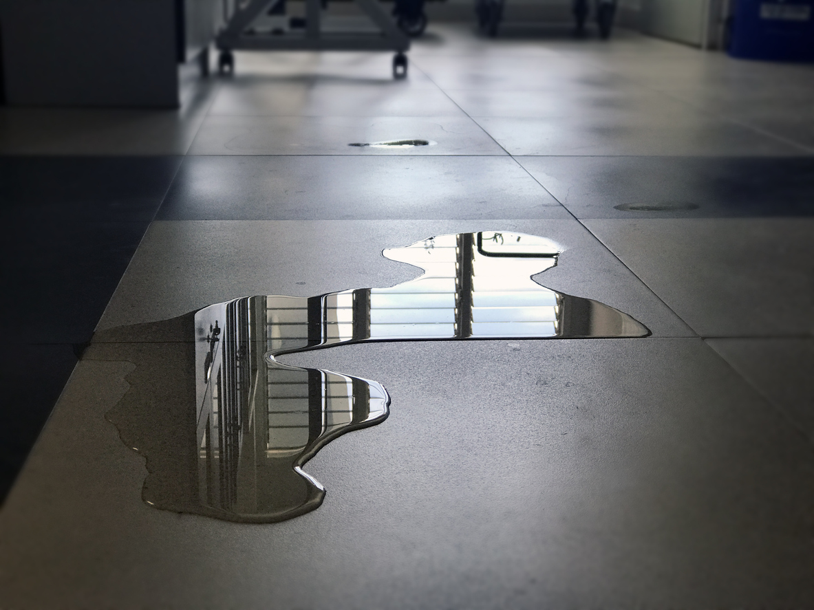 Close-up of spilled water leak on the floor of building. Wet floor from rainy splash or pipelines water leakage in office. Danger accident at home from liquid slippery floor hazard concept.